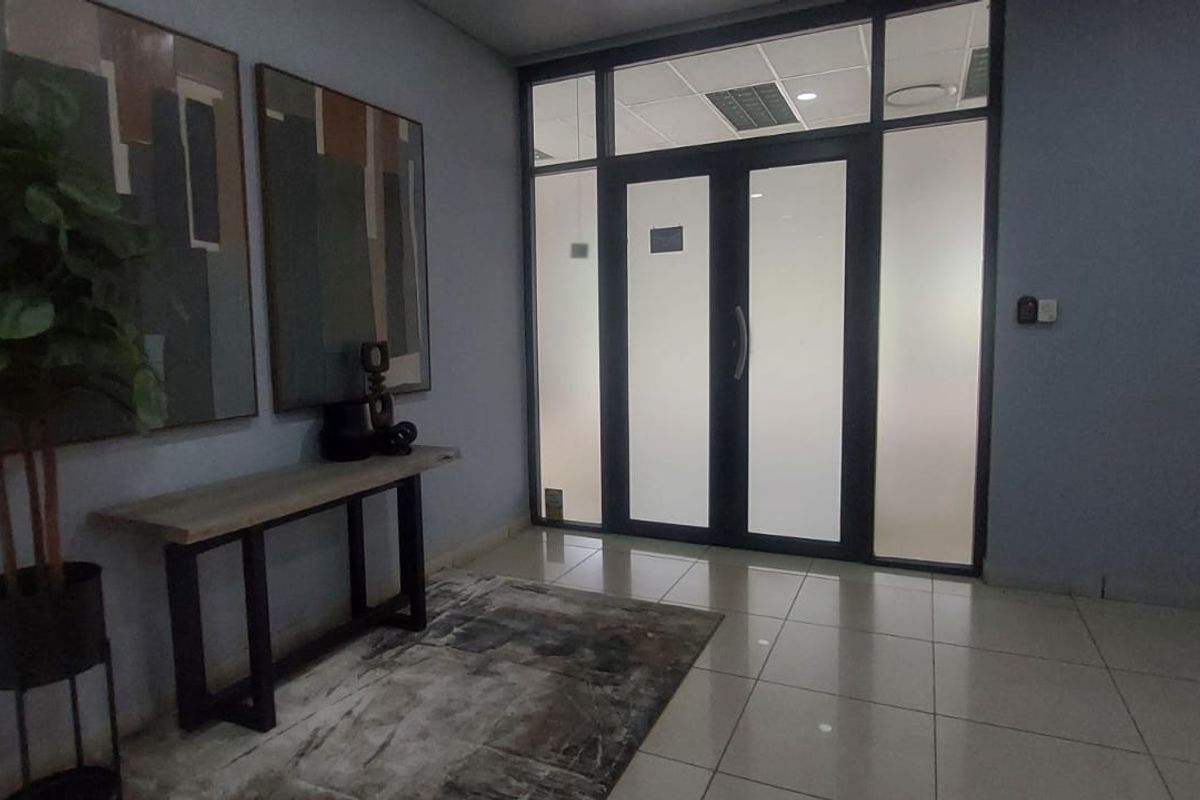A professional office entry area featuring tiled flooring, a suspended ceiling with recessed lighting, and modern frosted glass double doors.