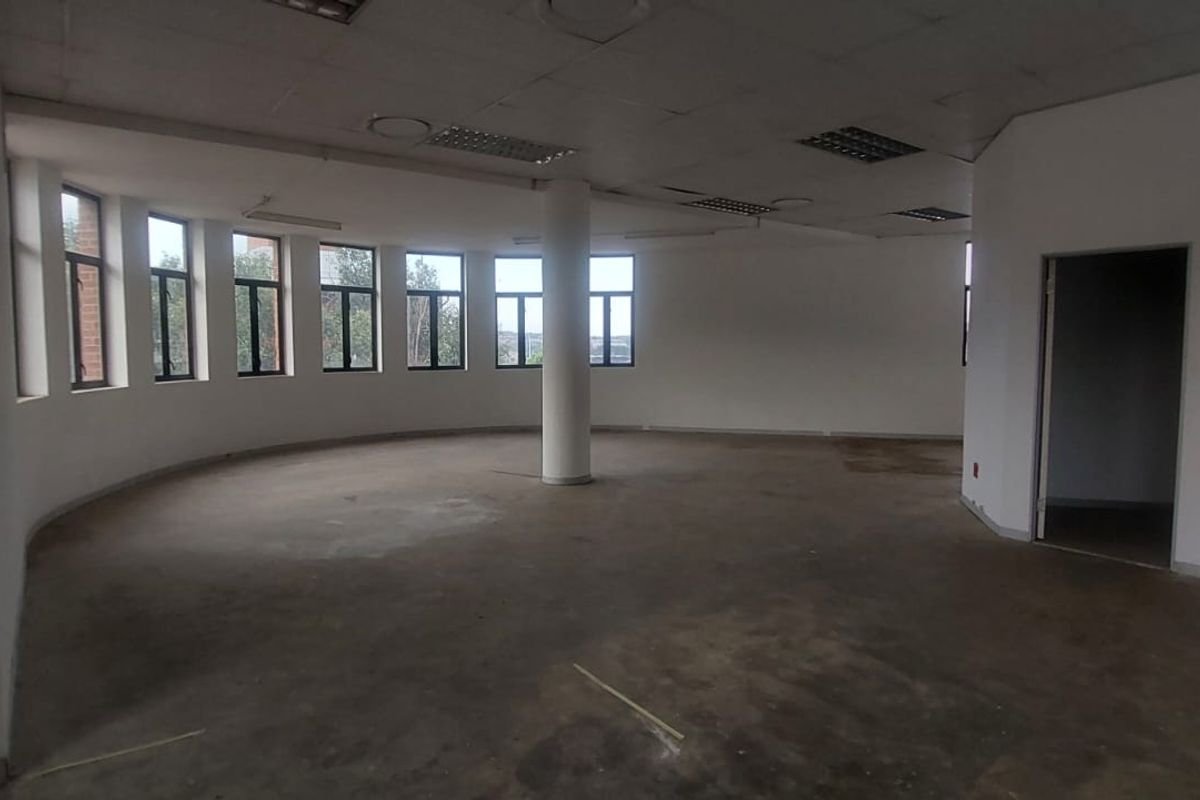 An expansive, vacant open-plan office space featuring a curved wall with large windows, a central structural column, and a suspended ceiling.