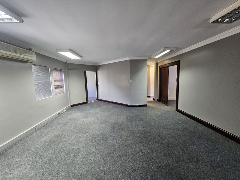 Spacious office area featuring grey carpeting, recessed lighting, wall-mounted air conditioning unit, and multiple access points to adjacent rooms.