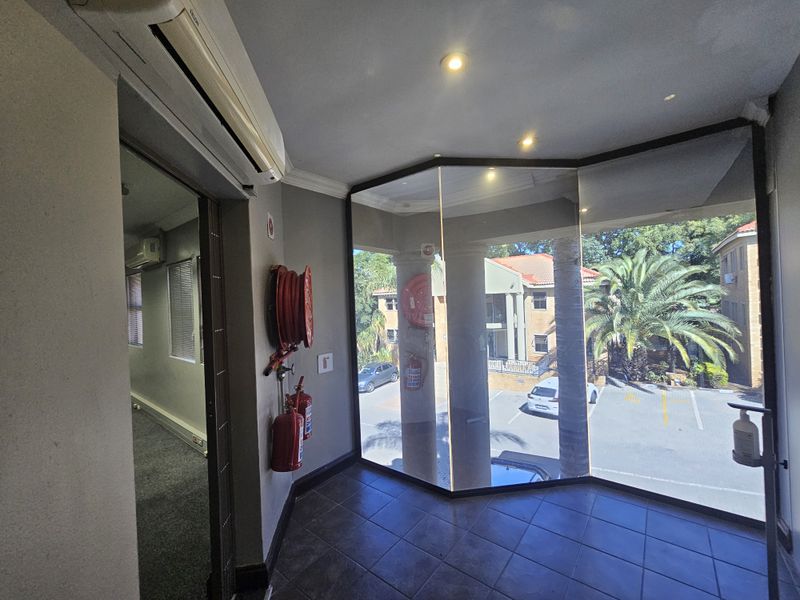 A bright office entrance area featuring large floor-to-ceiling windows, tiled flooring, wall-mounted fire safety equipment, and a split-system air conditioning unit.
