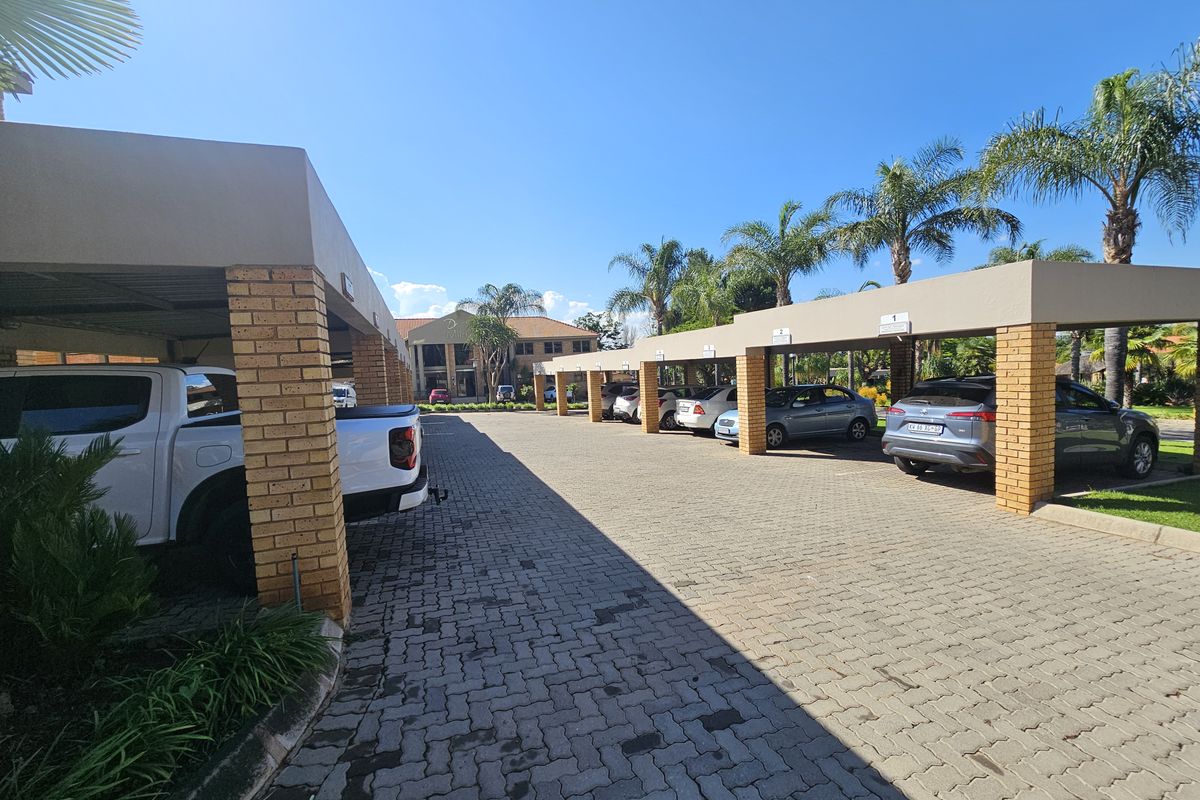 Covered parking area with brick pillars and paved driveway, providing sheltered vehicle storage for the office property.