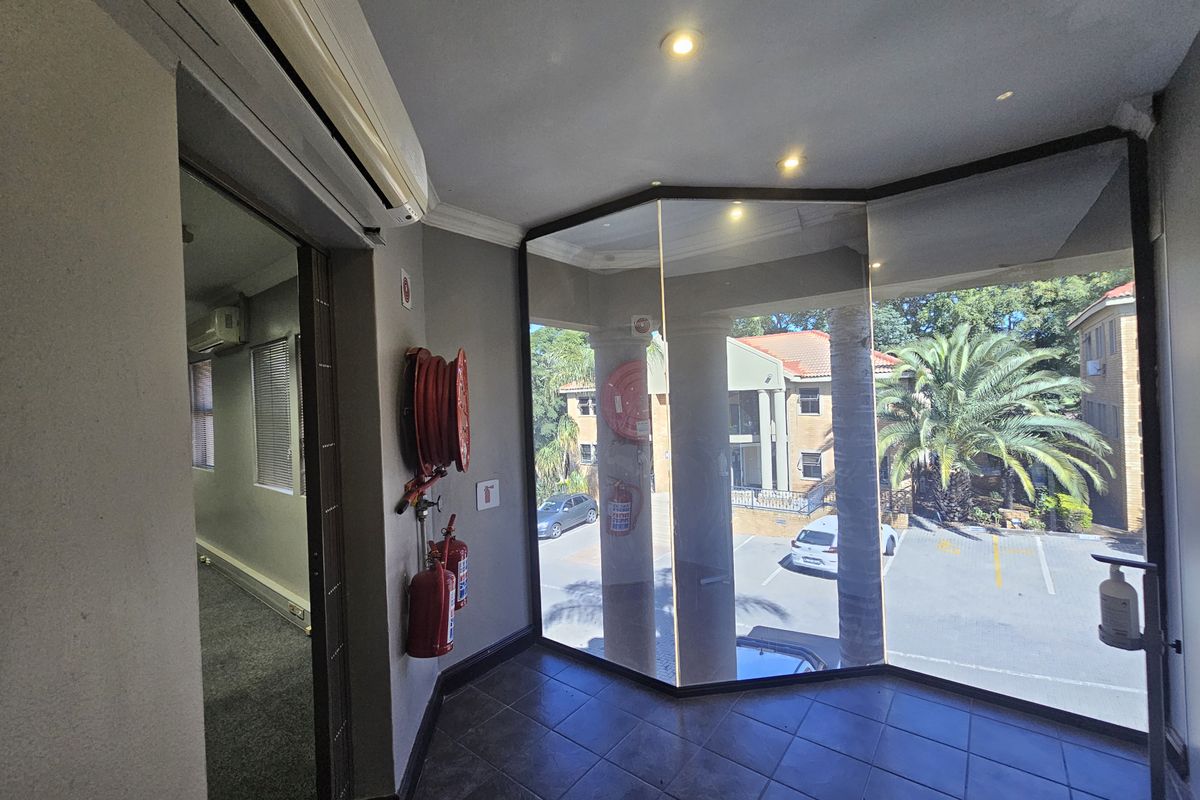 A bright office entrance area featuring large floor-to-ceiling windows, tiled flooring, wall-mounted fire safety equipment, and a split-system air conditioning unit.