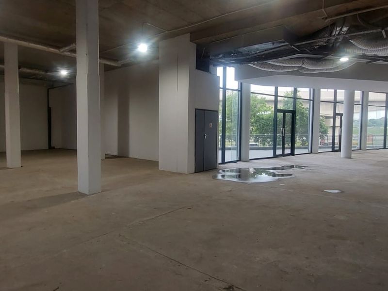 Expansive open-plan retail space featuring exposed industrial ceilings, structural columns, and large glass windows providing ample natural light.