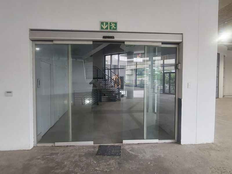 An open-plan retail entry area featuring automatic sliding glass doors, exposed concrete ceilings, and structural columns in a shell condition.