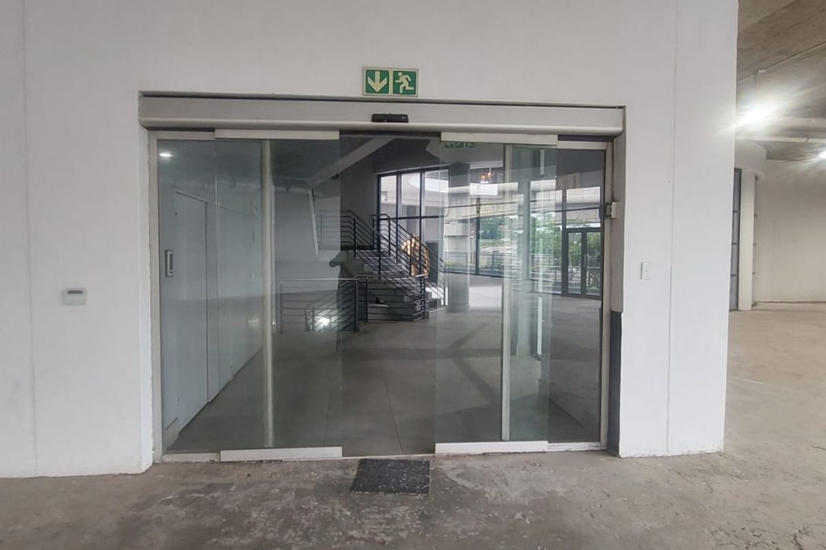 An open-plan retail entry area featuring automatic sliding glass doors, exposed concrete ceilings, and structural columns in a shell condition.