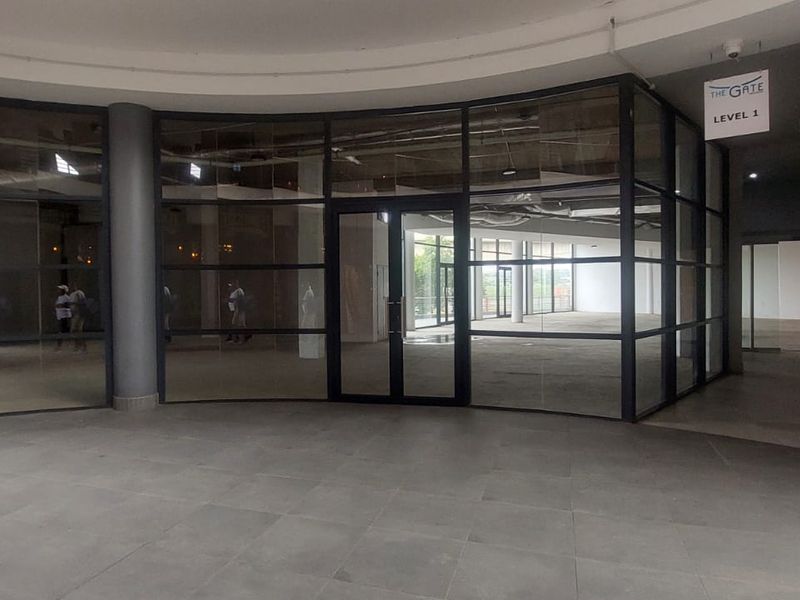 A modern commercial retail entrance featuring a curved glass storefront, tiled flooring, and structural columns, providing an open and professional facade.