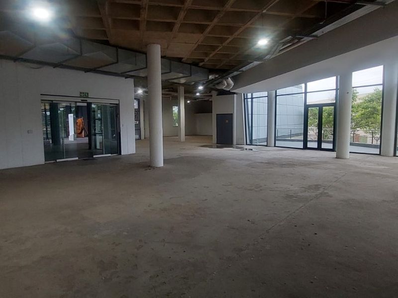 Spacious open-plan retail area featuring an exposed waffle slab ceiling, structural columns, and extensive floor-to-ceiling glass windows providing ample natural light.