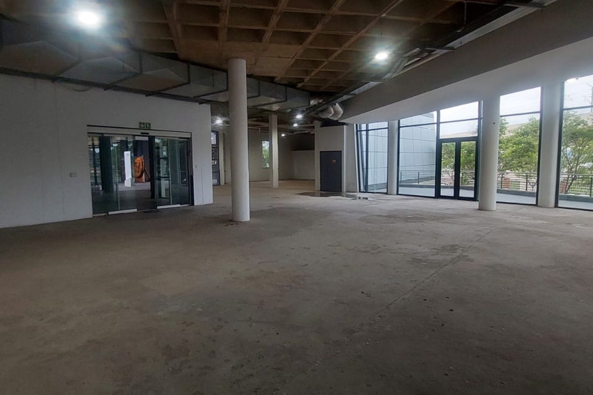 Spacious open-plan retail area featuring an exposed waffle slab ceiling, structural columns, and extensive floor-to-ceiling glass windows providing ample natural light.