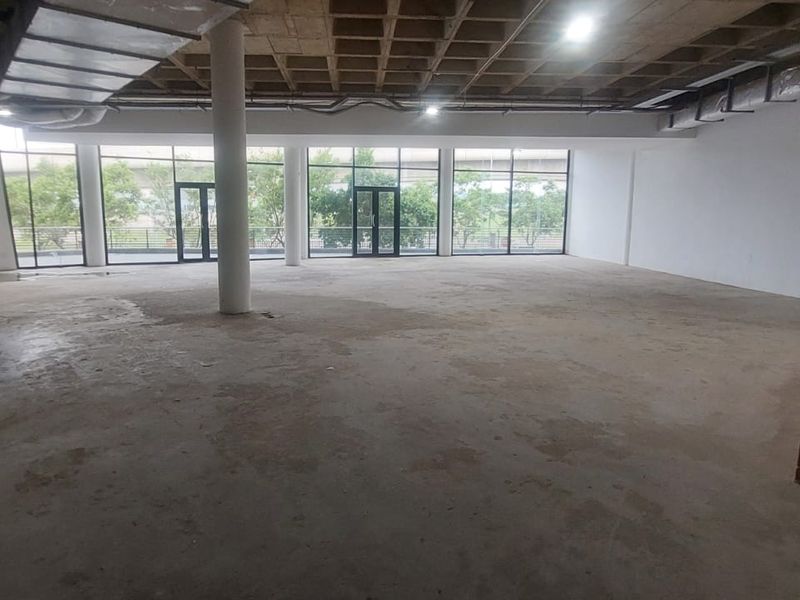 Spacious open-plan retail or commercial unit featuring an industrial aesthetic with exposed concrete waffle ceilings, ductwork, and large floor-to-ceiling windows.