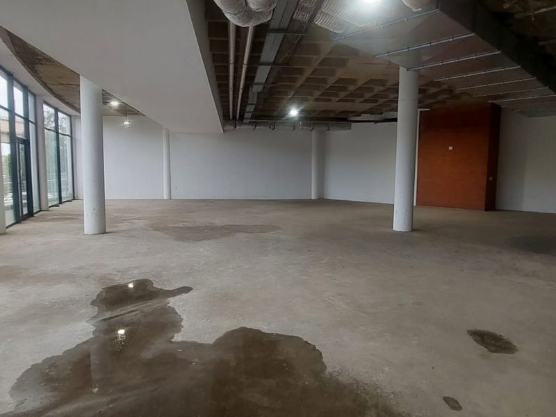 Expansive open-plan retail space featuring exposed industrial ceilings, structural columns, and floor-to-ceiling glass windows, currently in a shell condition.
