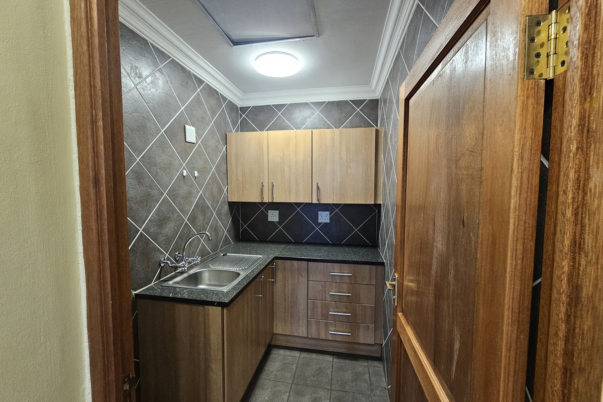 A compact kitchenette featuring built-in wooden cabinetry, dark granite countertops, a stainless steel sink, and tiled wall finishes.