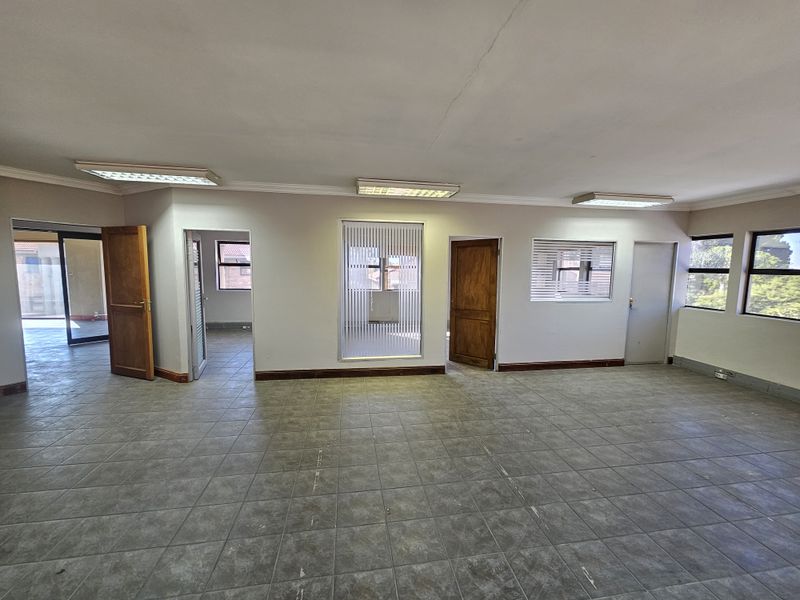 Spacious office area featuring tiled flooring, recessed fluorescent lighting, and multiple access points with wooden doors and frosted glass panels.