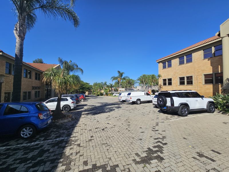 Exterior view of a commercial office complex featuring brick facade buildings, paved parking area, and established landscaping.