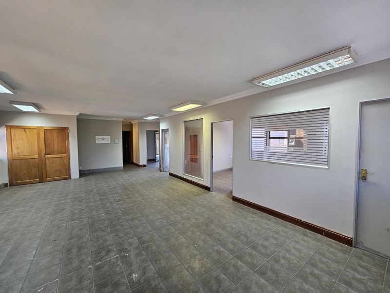 Spacious open-plan office area featuring tiled flooring, recessed fluorescent lighting, and multiple partitioned doorways leading to additional workspace.