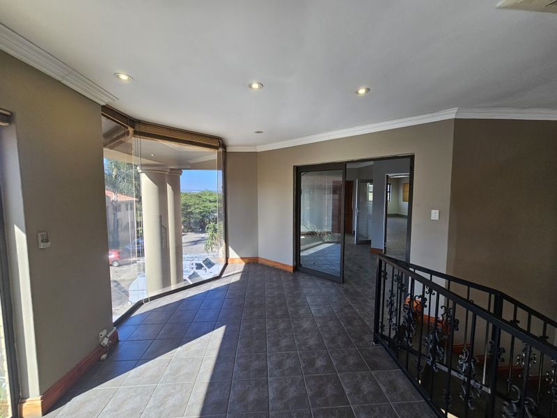 Spacious office landing area featuring tiled flooring, recessed ceiling lighting, large glass windows, and a decorative wrought iron staircase railing.