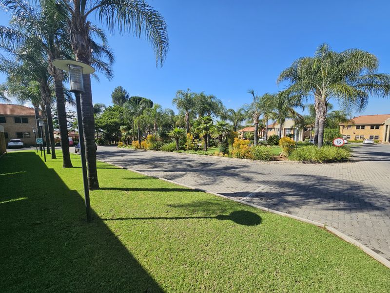 A well-maintained office park exterior featuring paved driveways, manicured lawns, and mature palm trees under a clear blue sky.