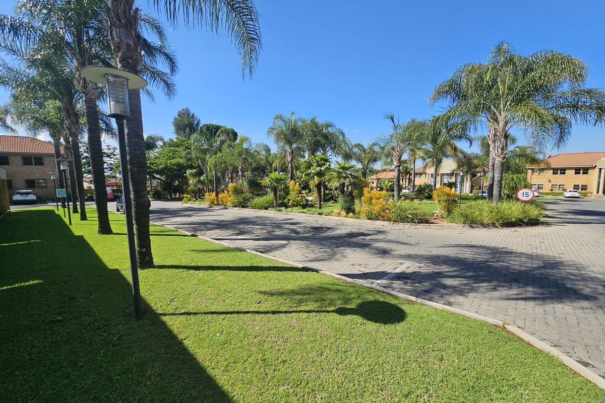 A well-maintained office park exterior featuring paved driveways, manicured lawns, and mature palm trees under a clear blue sky.