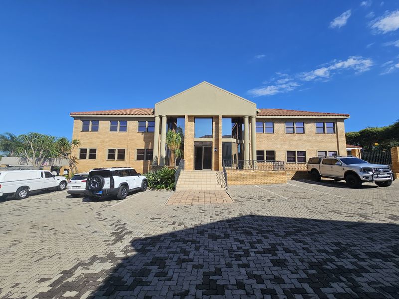 A professional two-story brick office building featuring a central entrance with columns, tiled roof, and paved parking area.