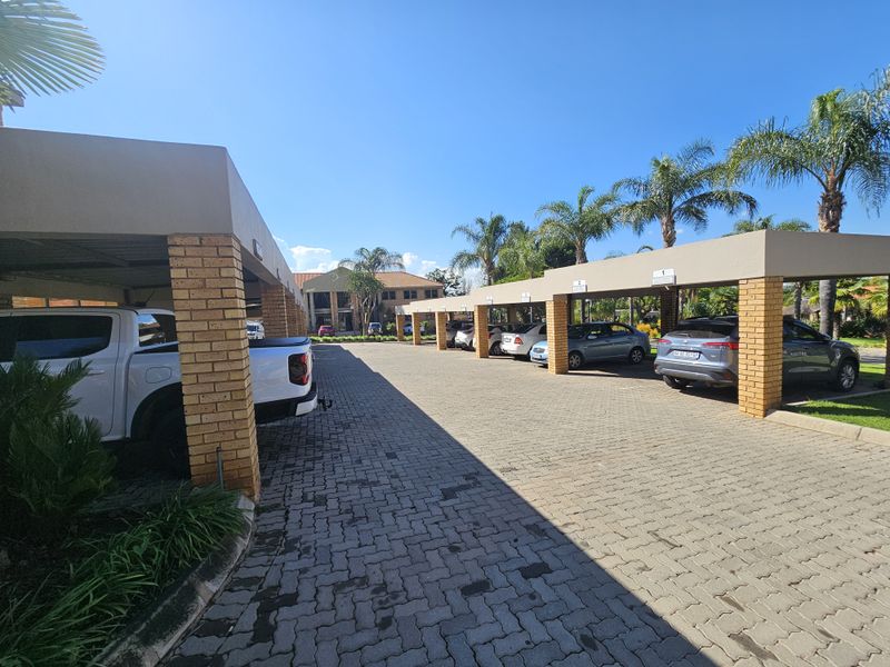 Covered parking area with brick pillars and paved driveway, providing sheltered vehicle storage for the office property.