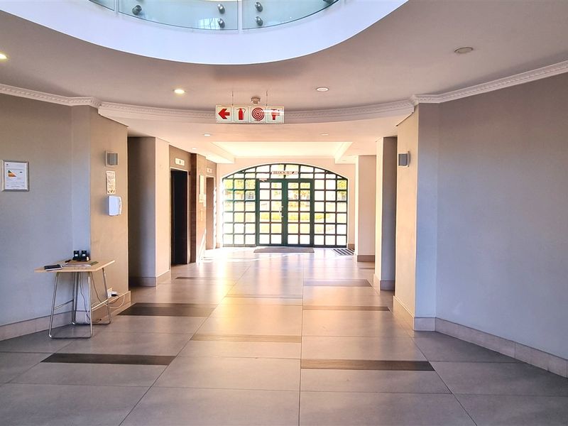 Spacious office building entrance lobby featuring tiled flooring, recessed ceiling lighting, a central skylight, and a large glass-paneled entrance door.
