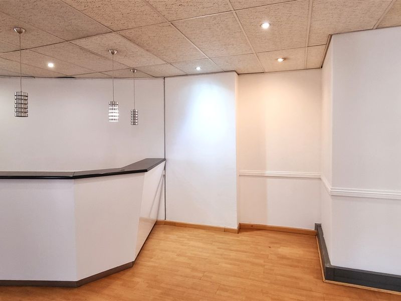 A clean, empty office reception area featuring a built-in desk, drop ceiling with recessed lighting, and laminate flooring.