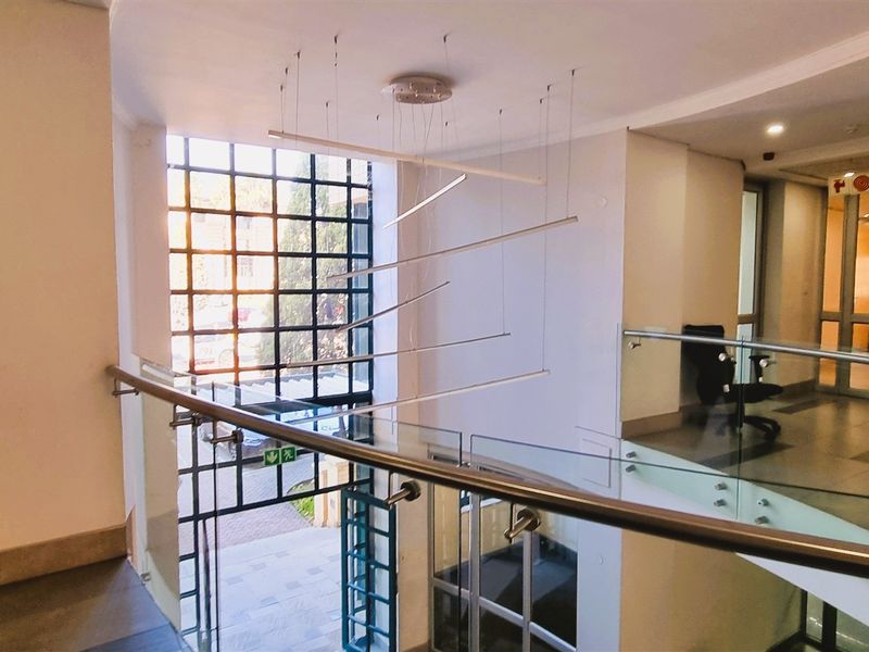 A bright and modern office building entrance lobby featuring a glass balustrade, tiled flooring, and a large feature window with natural light.