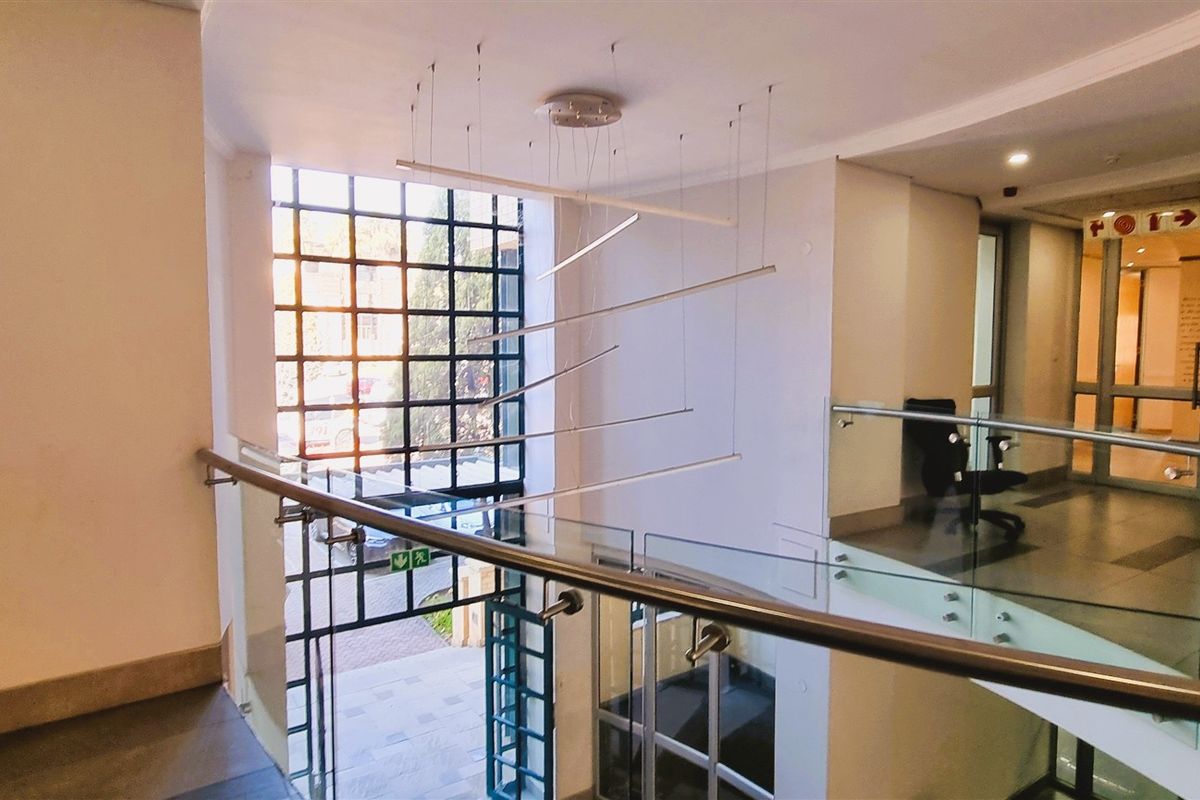 A bright and modern office building entrance lobby featuring a glass balustrade, tiled flooring, and a large feature window with natural light.