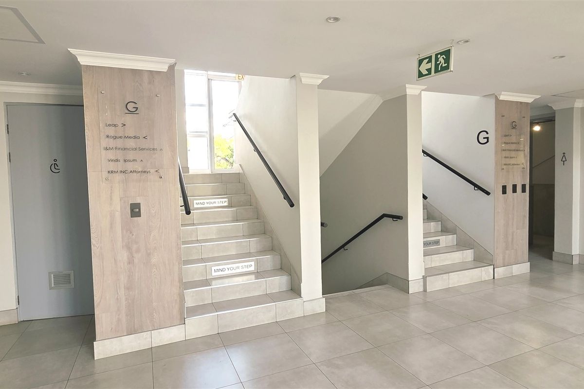A clean, modern office building hallway featuring tiled floors, dual staircases with handrails, and clear directional signage for tenants.