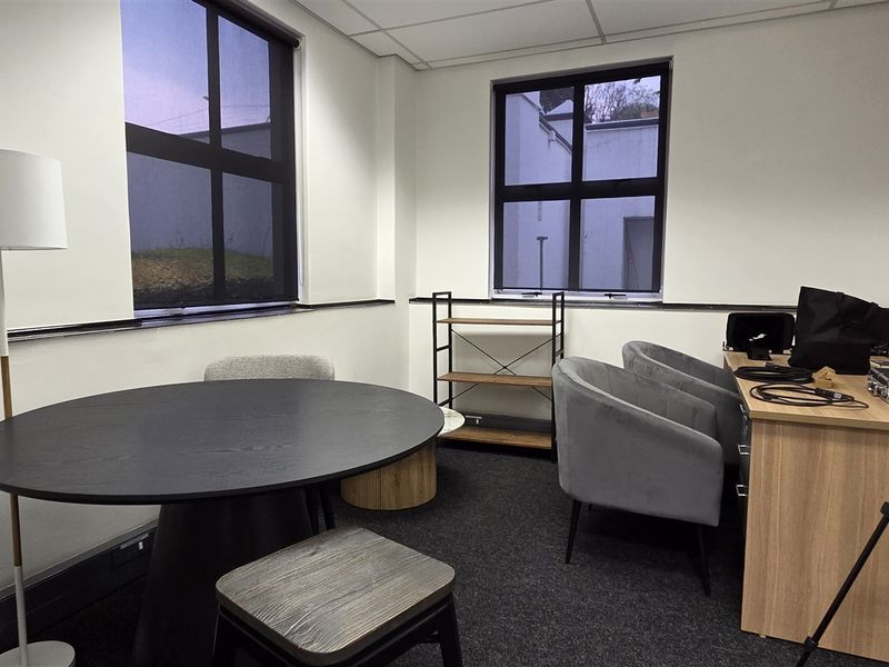 A functional office space featuring dark carpet flooring, suspended ceiling tiles, and large black-framed windows providing natural light.