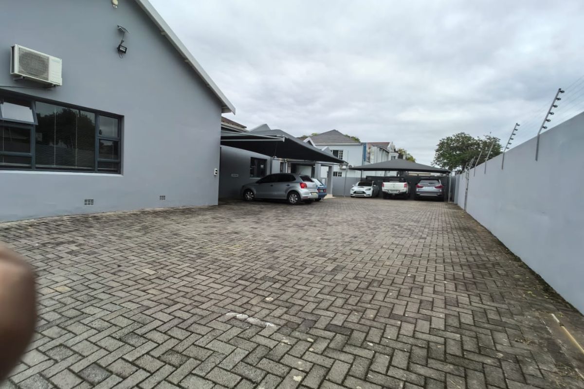 Rear exterior view of the commercial property featuring a large paved parking area, covered carports, and secure perimeter wall with electric fencing.