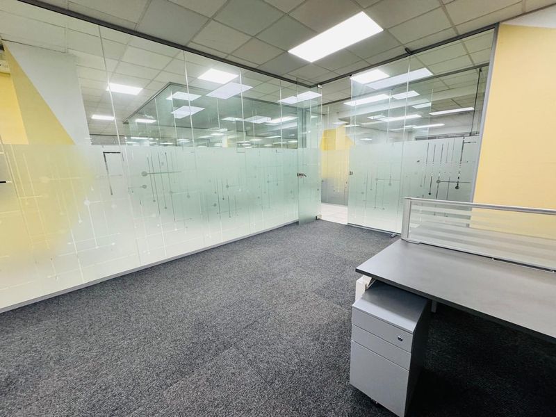 Modern office space featuring glass partition walls with frosted privacy detailing, recessed ceiling lighting, and durable carpet tiles.