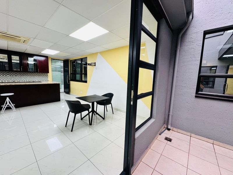 Modern open-plan office space featuring a kitchenette with dark cabinetry, granite countertops, tiled flooring, and direct access to an outdoor patio area.