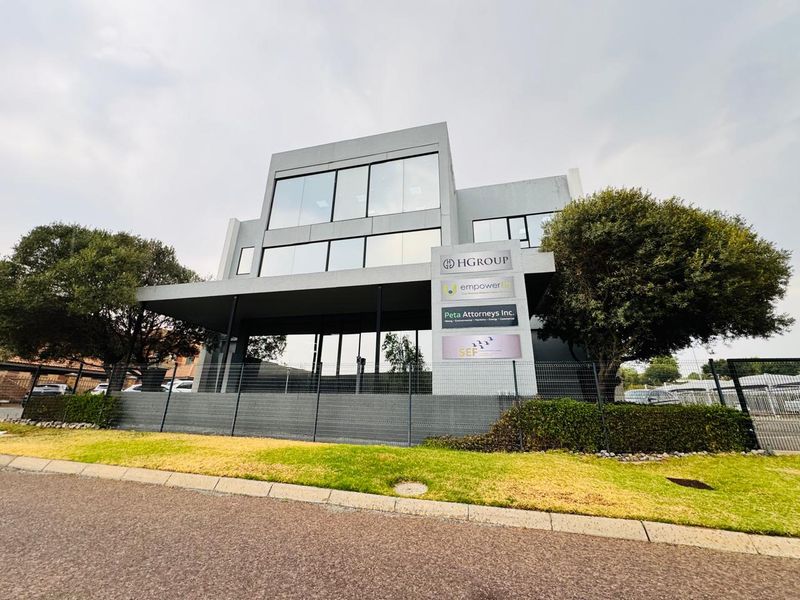 Modern multi-level office building featuring a prominent glass facade and professional business signage, situated behind secure perimeter fencing.