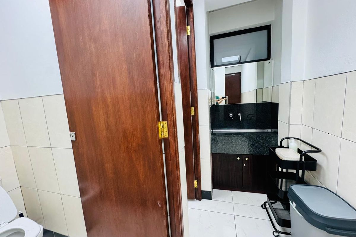 A functional office bathroom featuring a granite vanity countertop, built-in cabinetry, and neutral ceramic tiling throughout.