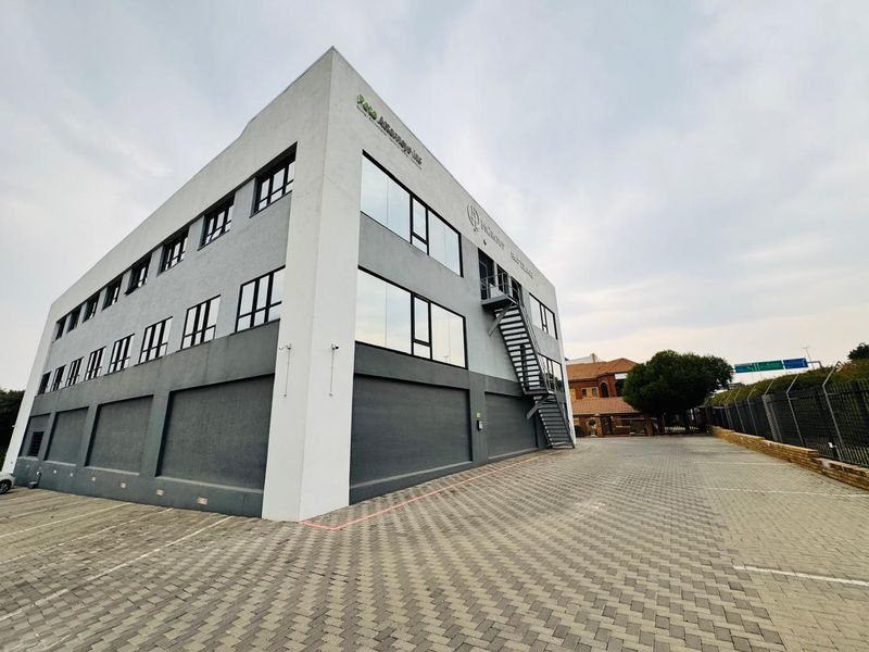 A modern multi-story office building featuring a paved parking area, external metal staircase, and large glass windows.