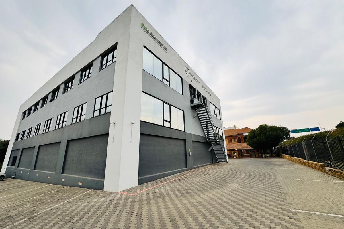 A modern multi-story office building featuring a paved parking area, external metal staircase, and large glass windows.