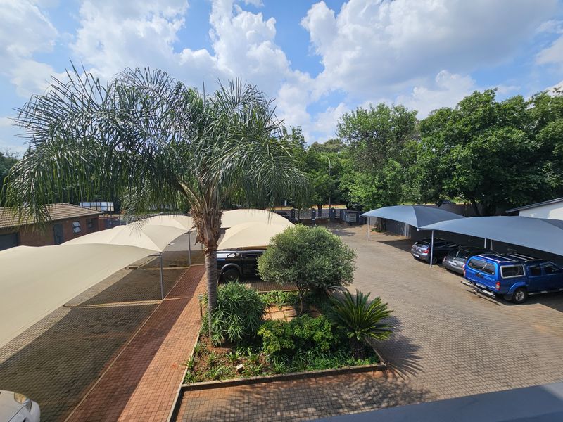 Elevated view of the office property parking area featuring paved surfaces, shade sail structures, and landscaped garden beds with mature trees.