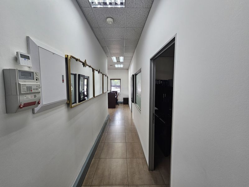 A functional office hallway featuring tiled flooring, a suspended acoustic ceiling with recessed lighting, and access to adjacent office spaces.