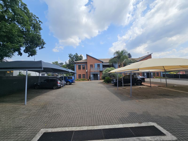 Exterior view of the office building entrance featuring paved parking area with shade cloth carports.