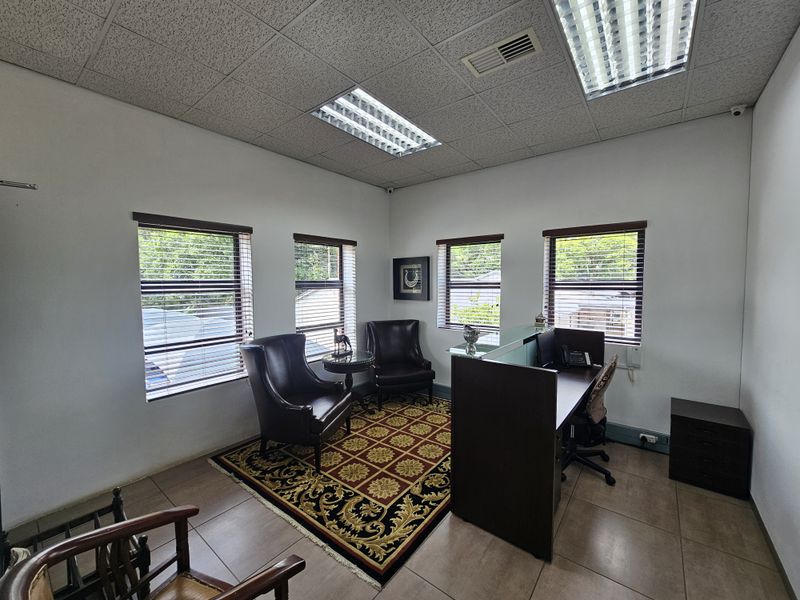 A functional office space featuring multiple windows with blinds, recessed fluorescent lighting, and tiled flooring, suitable for a professional work environment.