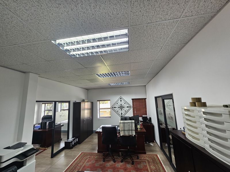 A functional office space featuring a suspended acoustic ceiling, recessed fluorescent lighting, tiled flooring, and glass-partitioned interior walls.