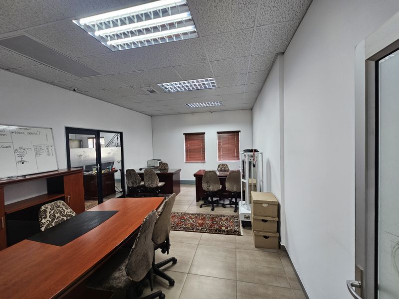 A functional office space featuring tiled flooring, recessed fluorescent lighting, and a glass partition wall, providing a professional work environment.