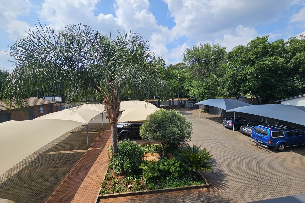 Elevated view of the office property parking area featuring paved surfaces, shade sail structures, and landscaped garden beds with mature trees.