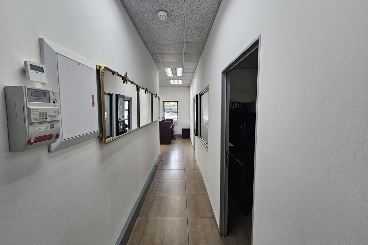 A functional office hallway featuring tiled flooring, a suspended acoustic ceiling with recessed lighting, and access to adjacent office spaces.