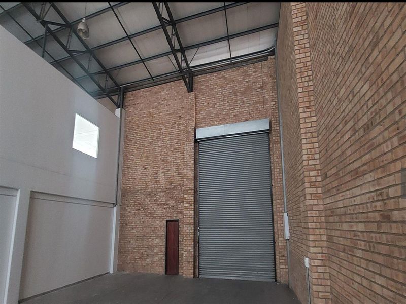 Spacious industrial utility area featuring high ceilings with exposed steel trusses, face brick walls, and a large roller shutter door for easy access.