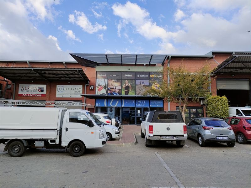 Front elevation of an industrial unit featuring a brick facade, metal canopy, and glass storefront entrance with dedicated parking.