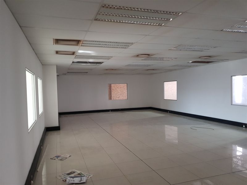 An open-plan office space featuring tiled flooring, white walls, and a suspended ceiling with recessed lighting.