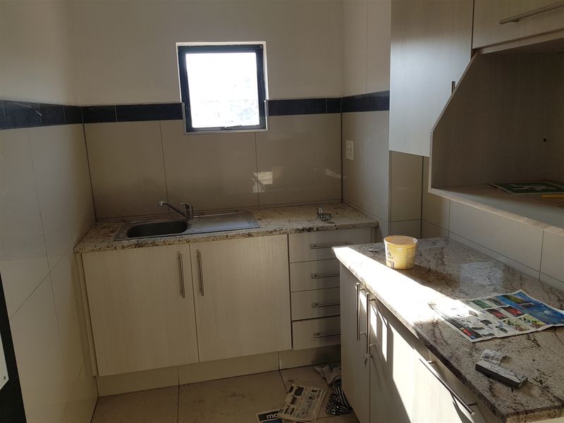 A functional scullery area featuring granite countertops, built-in cabinetry, and a stainless steel sink with tiled finishes.