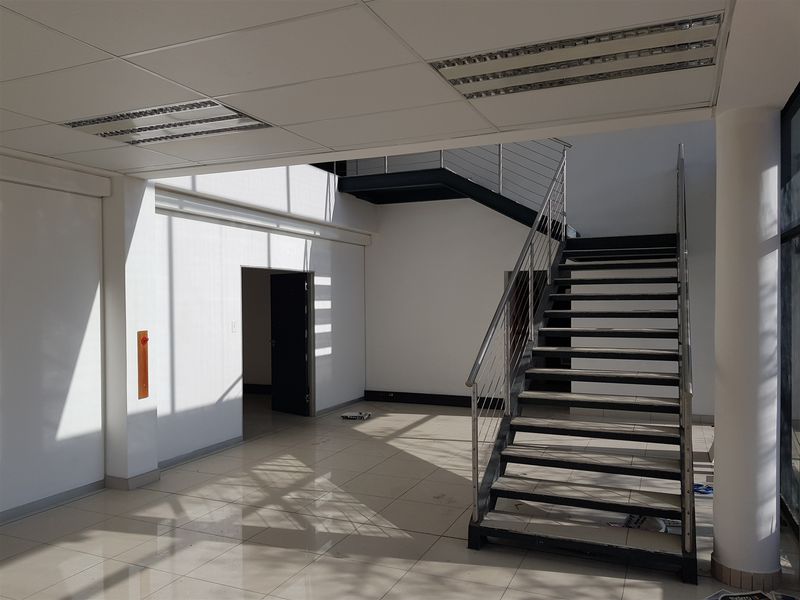 Spacious industrial entrance area featuring tiled flooring, a modern metal staircase with stainless steel balustrades, and a suspended ceiling with recessed lighting.