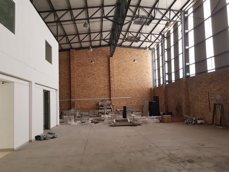Spacious industrial warehouse unit featuring high ceilings with exposed steel trusses, brick walls, concrete flooring, and large windows providing ample natural light.